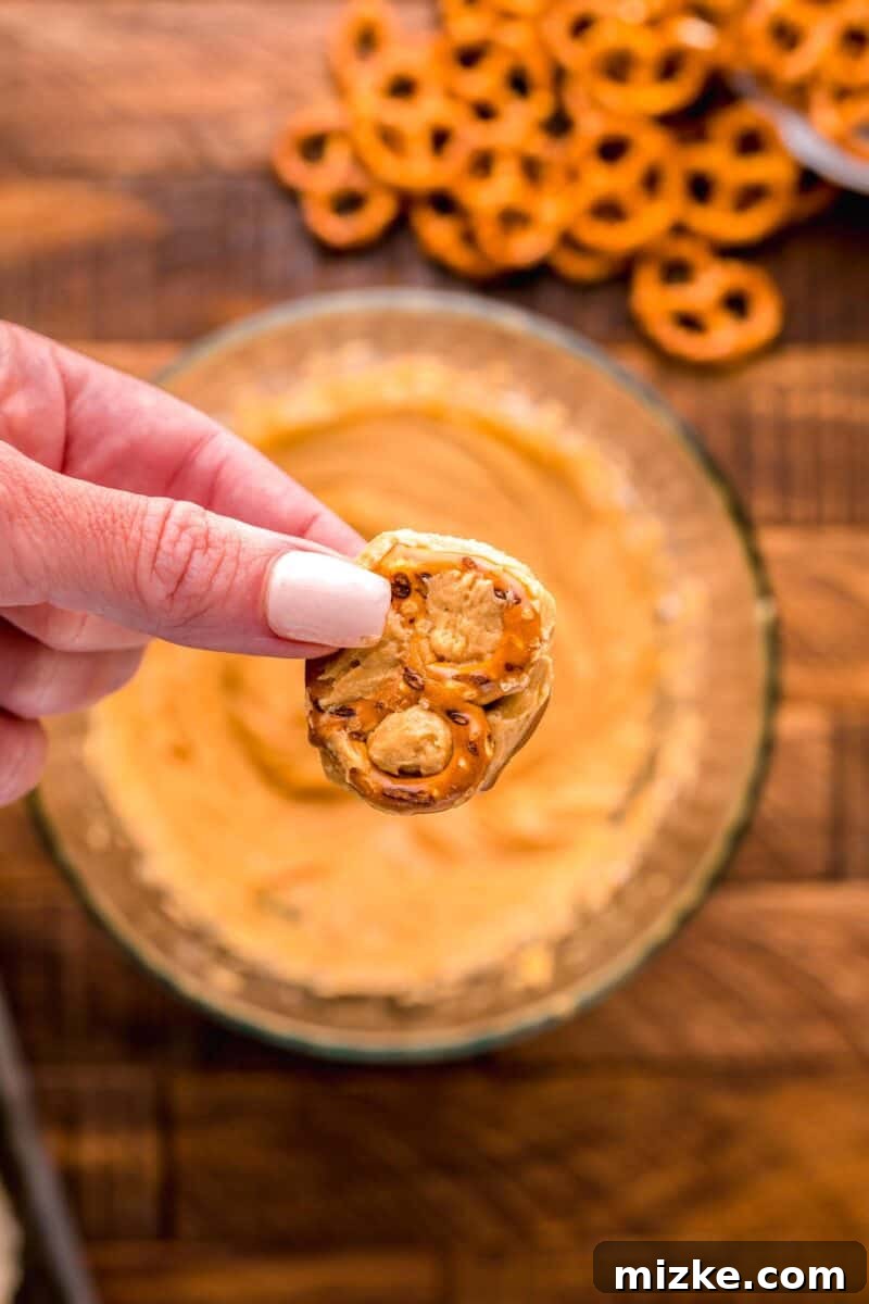 A mini pretzel with peanut butter mixture neatly sandwiched in the center, being held in the air by a hand, ready for the next step