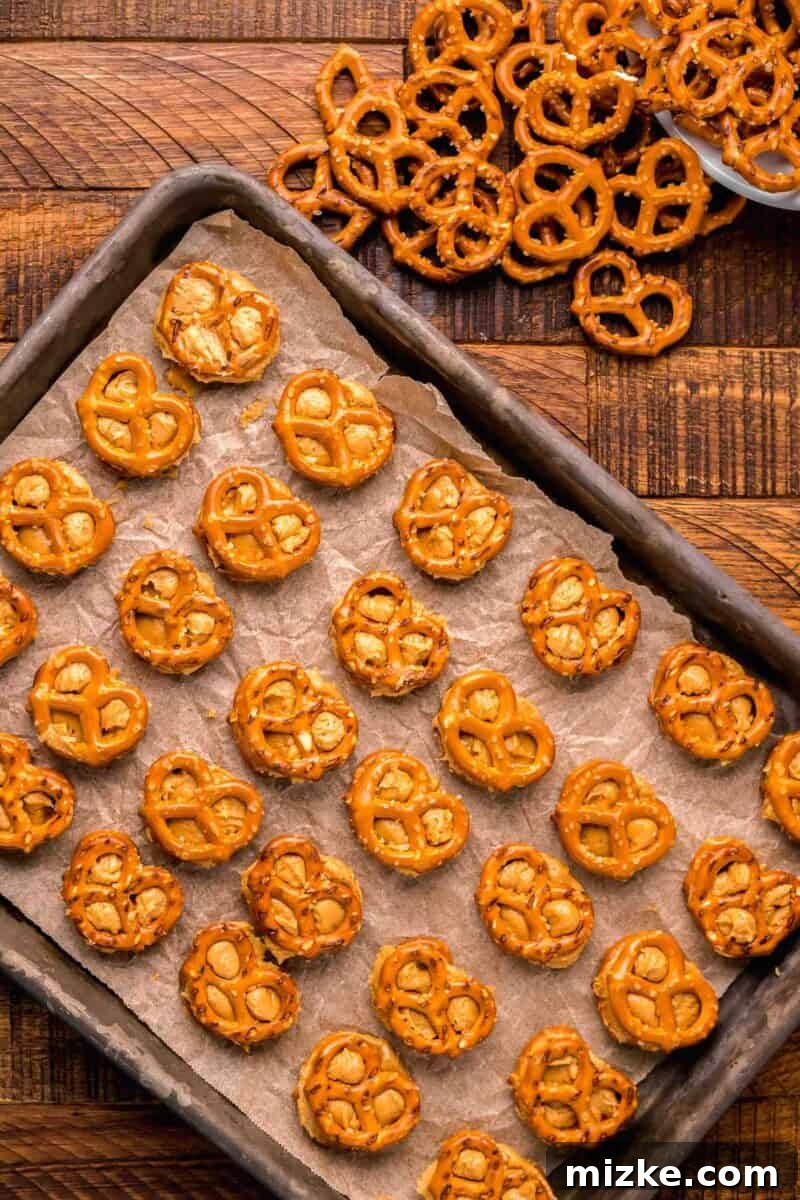 Assembled peanut butter pretzel bites neatly lined up on parchment paper covering a rimmed baking sheet, prepared for chilling