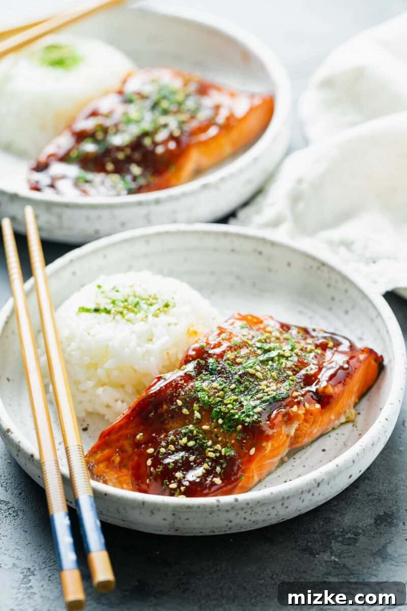 Perfect Air Fryer Teriyaki Salmon 2 Teriyaki glazed salmon on a speckled ceramic plate with furikake sprinkled on top, served alongside a mound of white rice and wooden chopsticks.