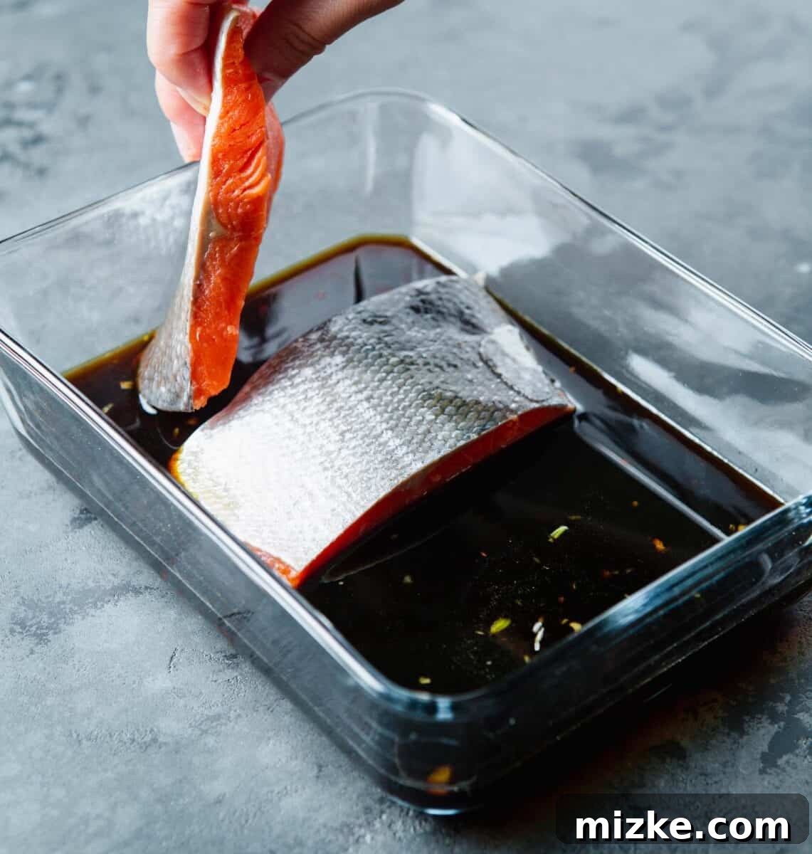 Perfect Air Fryer Teriyaki Salmon 6 Placing a salmon fillet, flesh side down, into the teriyaki marinade within a glass container, ready for marinating.