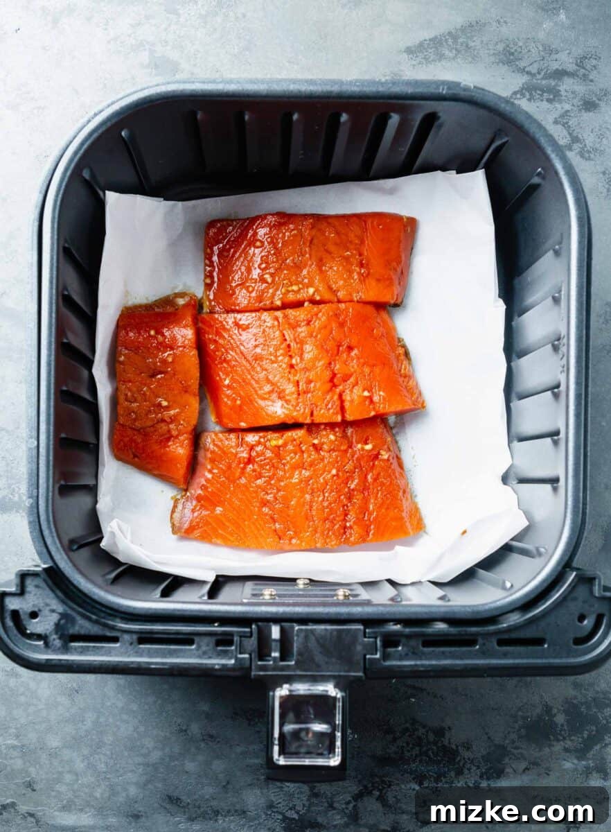 Perfect Air Fryer Teriyaki Salmon 7 Marinated salmon fillets resting on parchment paper inside the air fryer basket, ready for cooking.