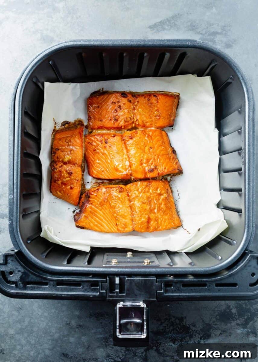 Perfect Air Fryer Teriyaki Salmon 8 Perfectly cooked salmon fillets in the air fryer basket on top of parchment paper, glazed and ready to be served.