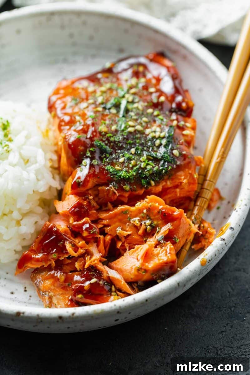 Perfect Air Fryer Teriyaki Salmon 9 Teriyaki glazed salmon fillet broken into large, flaky pieces on a speckled ceramic plate, with wooden chopsticks resting nearby.