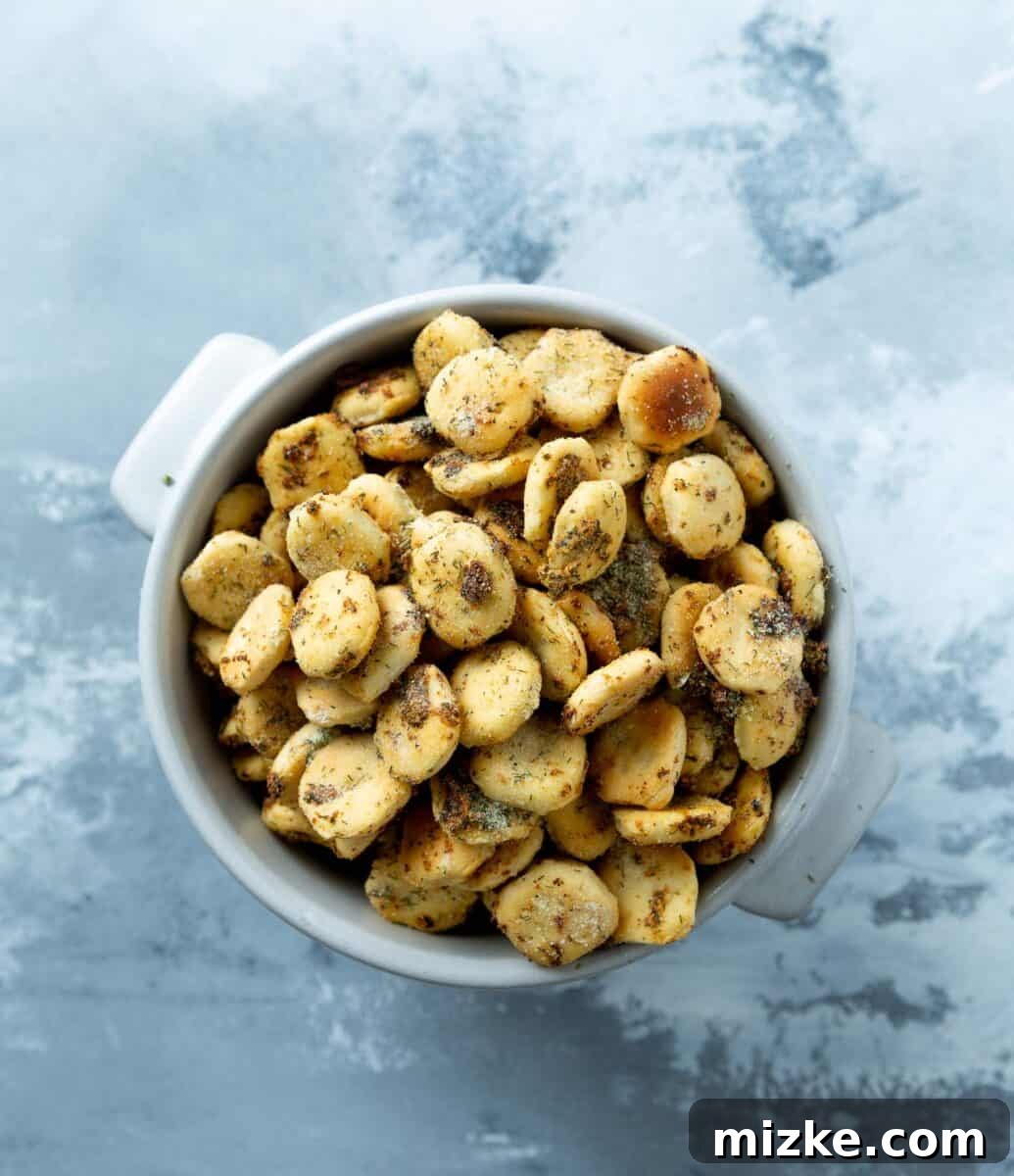 A small, elegant bowl overflowing with golden, perfectly seasoned ranch oyster crackers on a rustic grey background.