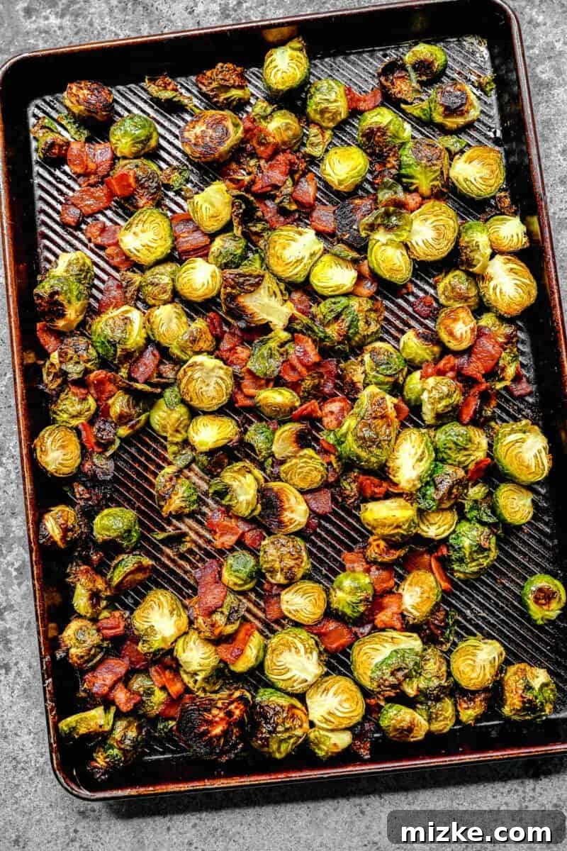 Golden Bacon Roasted Brussels Sprouts 7 Golden brown roasted brussels sprouts mixed with crispy bacon pieces on a rimmed baking sheet, just out of the oven.