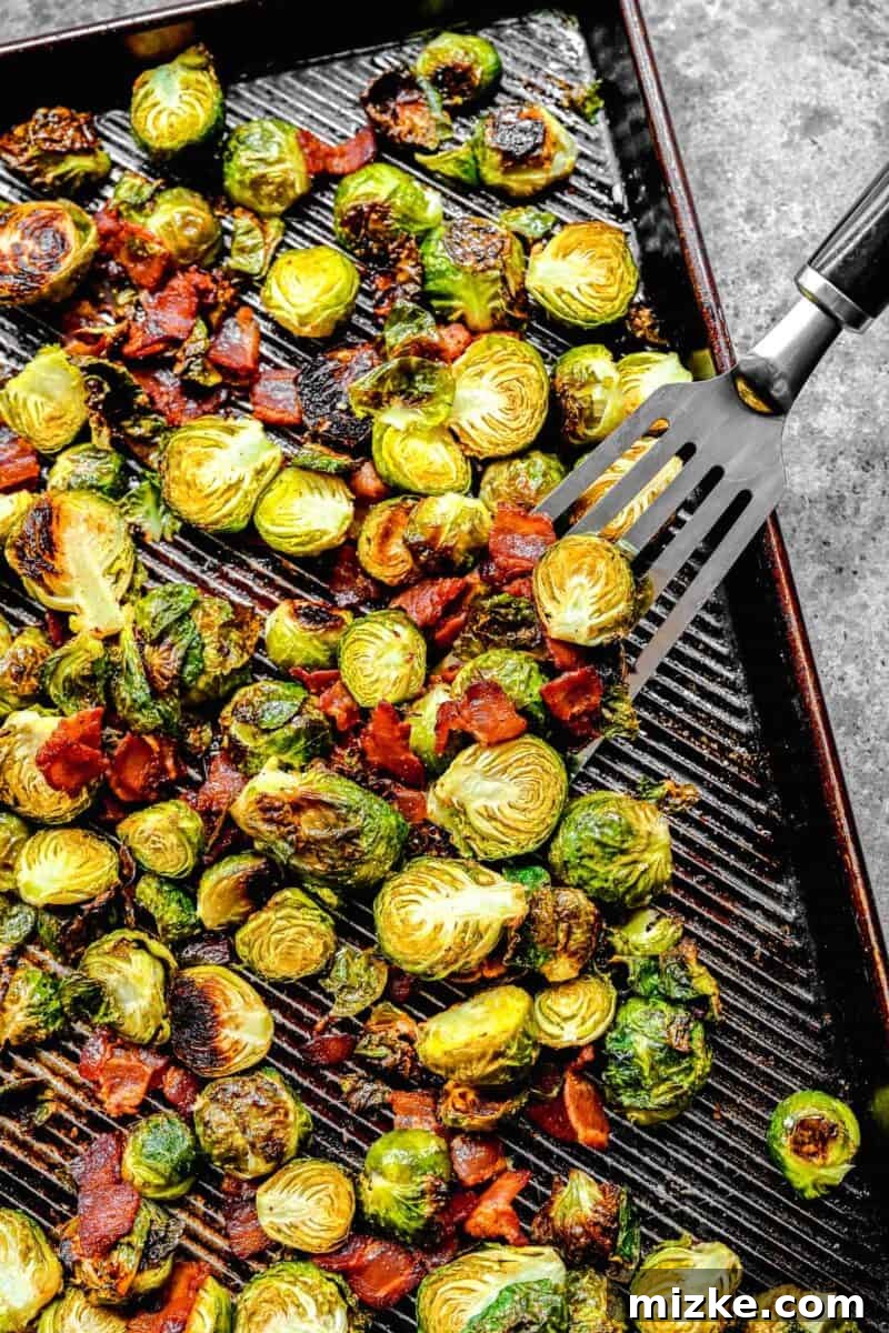 Golden Bacon Roasted Brussels Sprouts 8 A metal fish spatula scooping up a generous portion of roasted brussels sprouts and crispy bacon from a rimmed baking sheet.