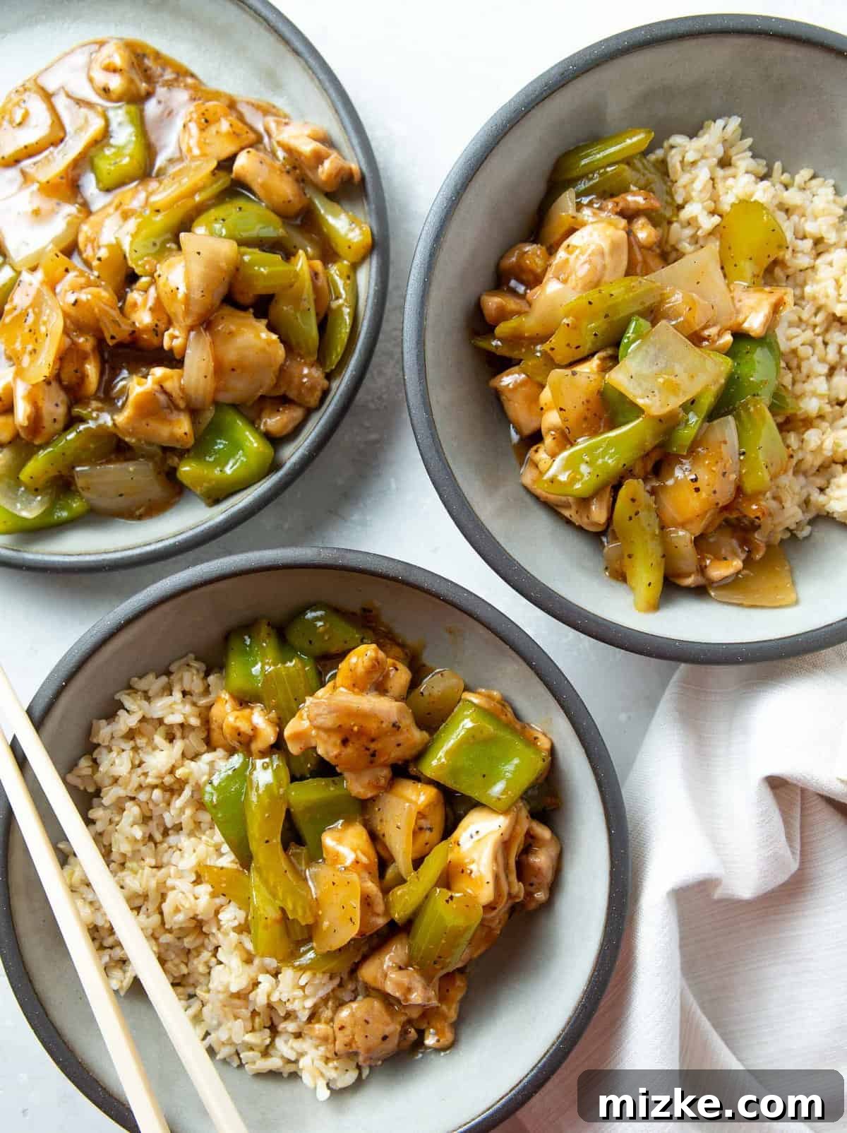 Restaurant-Quality Black Pepper Chicken 2 A tantalizing serving of homemade black pepper chicken with brown rice in elegant grey bowls, ready to be enjoyed with plastic chopsticks.