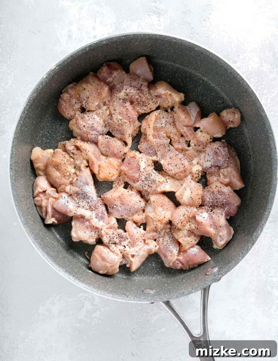 Restaurant-Quality Black Pepper Chicken 7 Cubed chicken thighs browning in a grey nonstick skillet, seasoned with black pepper and salt, developing a delicious sear.