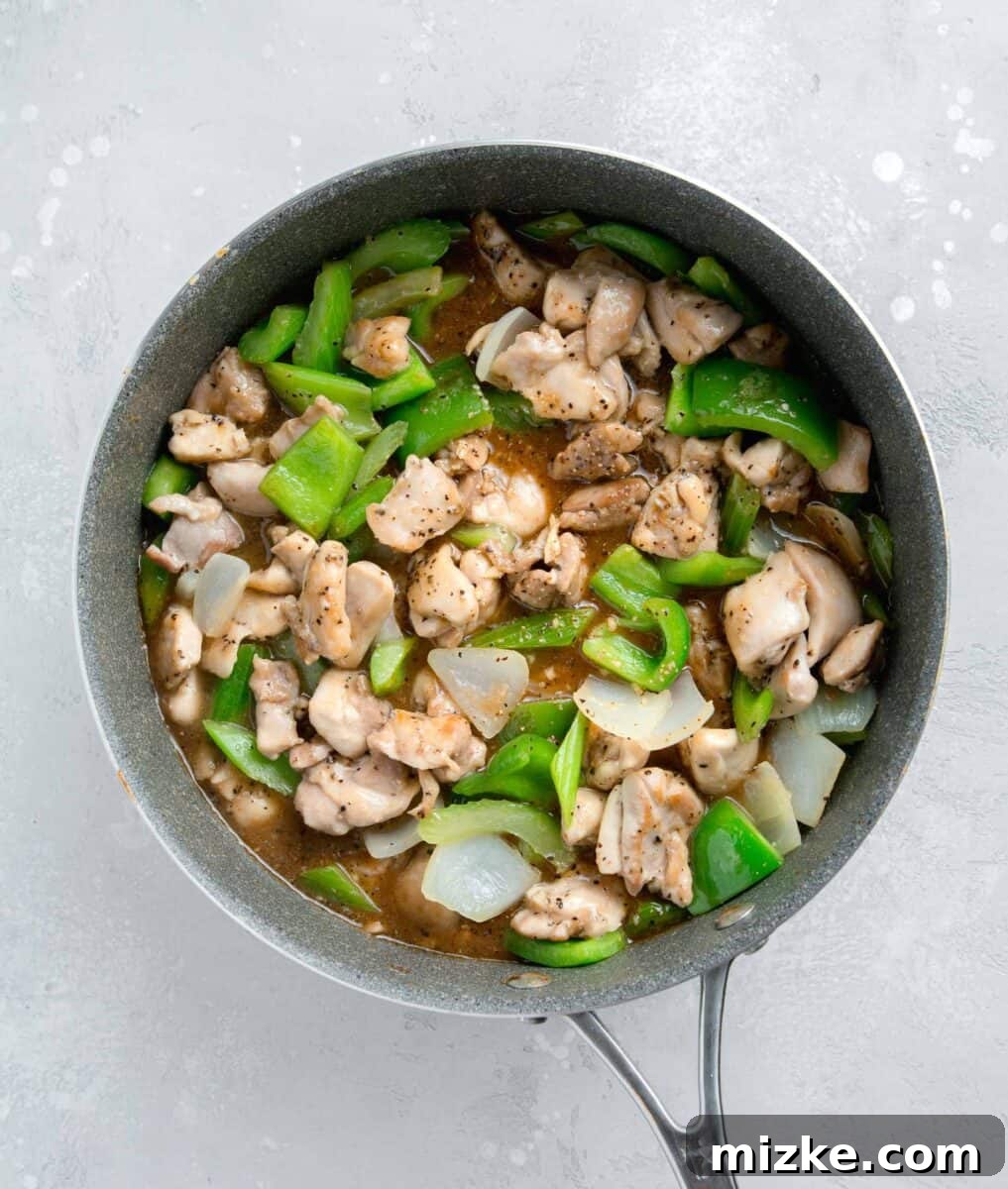 Restaurant-Quality Black Pepper Chicken 10 The rich black pepper sauce being poured over the chicken and vegetable mixture in the skillet, about to thicken and coat everything beautifully.