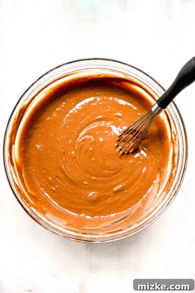 Decadent Chocolate Pudding Poke Cake 5 Thoroughly mixed chocolate cake batter, smooth and consistent, with a whisk resting in the clear bowl.