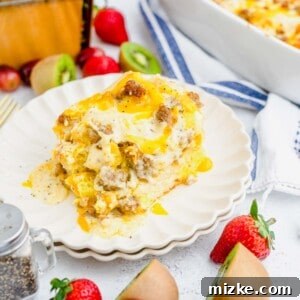 a generous portion of biscuits and gravy casserole on a white scalloped plate with cherries, kiwis, and strawberries in the photo