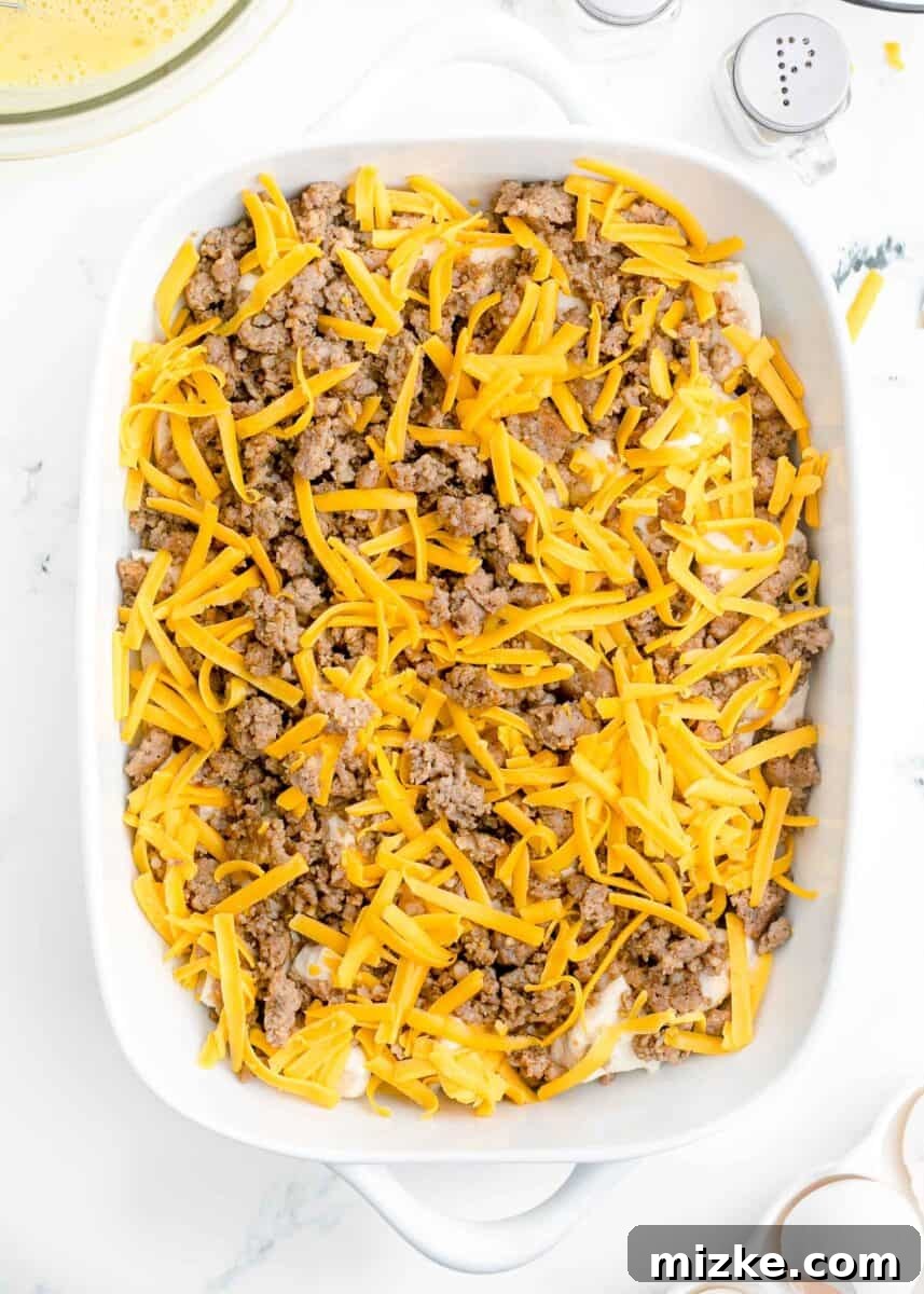 Southern Comfort Biscuit Bake 7 shredded cheese sprinkled on top of browned sausage and biscuits in a white baking dish
