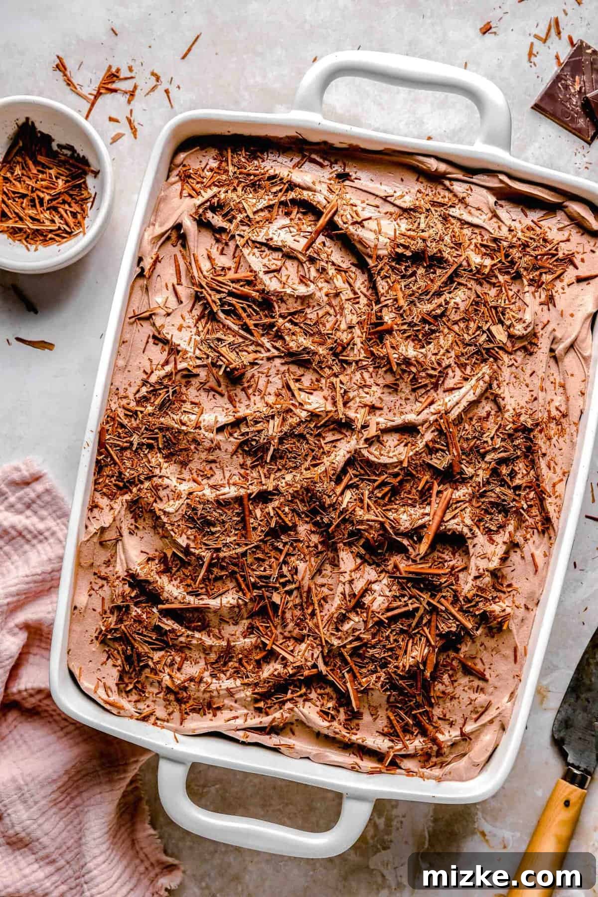 Chocolate cake is soaked in 3 kinds of milk and topped with chocolate Cool Whip and shaved chocolate in this spin on tres leches cake. A full chocolate tres leches cake, garnished with chocolate shavings, next to a bowl of extra shavings.