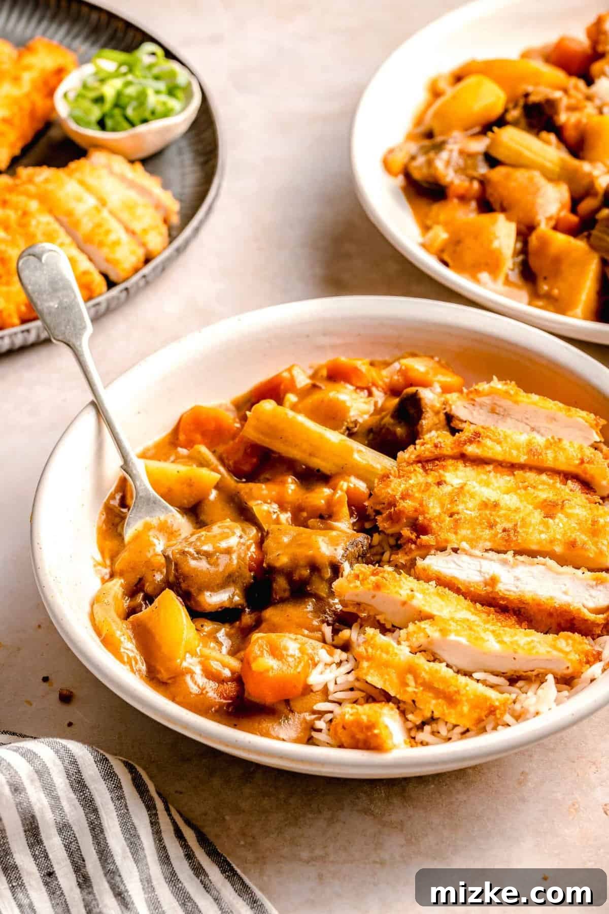 A feast of crispy chicken katsu and hearty Japanese beef curry awaits. Two enticing bowls of Chicken Katsu Curry, richly coated in curry sauce and served over rice, are presented alongside a platter of freshly fried chicken katsu slices, inviting a hearty meal.