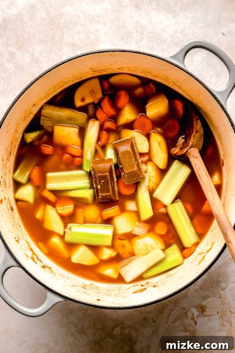 Adding curry cubes for authentic Japanese flavor. Japanese curry roux cubes being added to a simmering pot of vegetables and beef stock, ready to dissolve and thicken into a rich curry sauce.