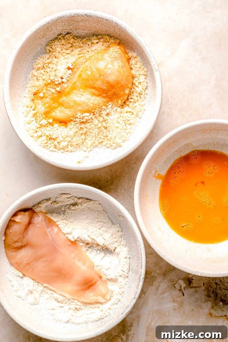 Perfectly breading chicken with panko for katsu. A chicken breast being coated in panko breadcrumbs as part of the breading station for preparing crispy chicken katsu.