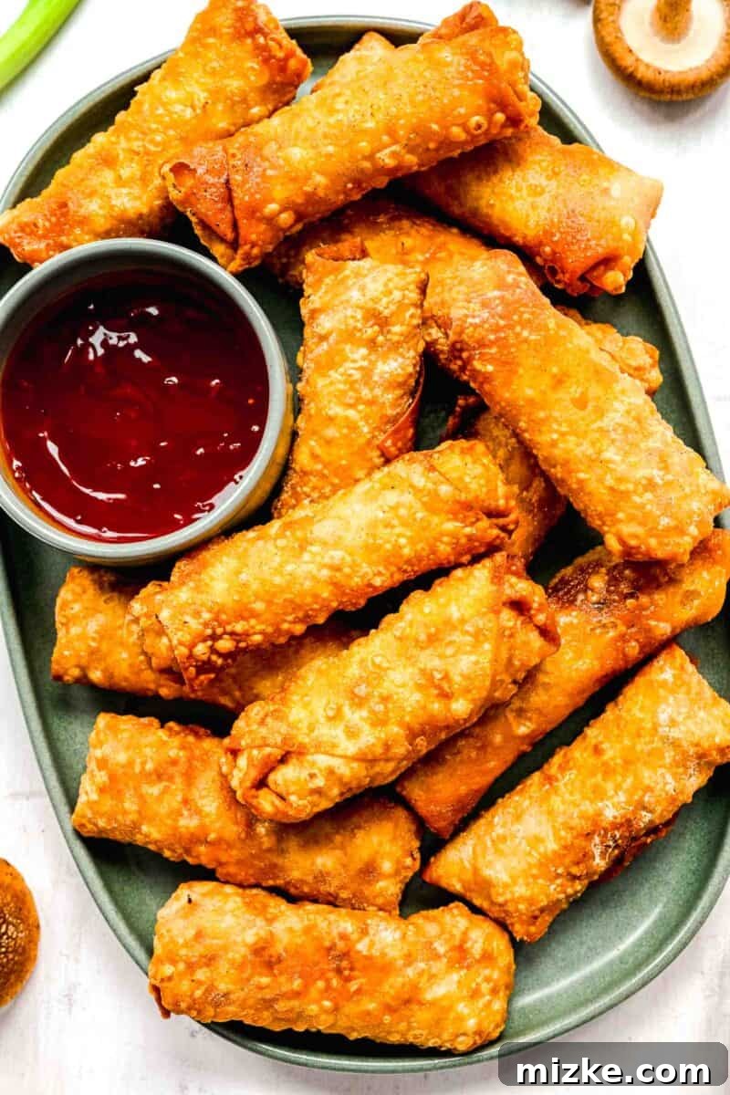 Crispy golden spring rolls on a plate with dipping sauce.