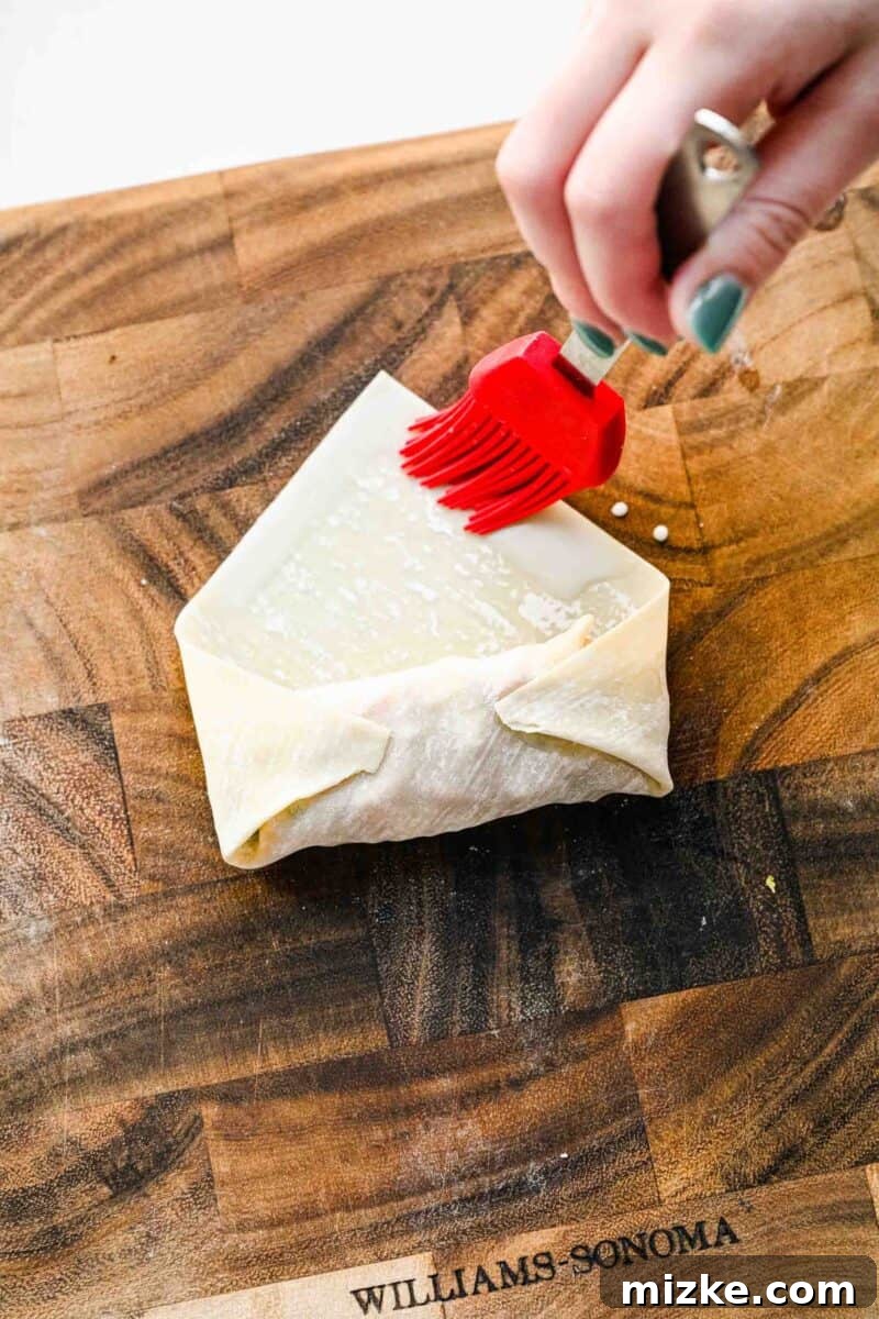 Brushing spring roll wrapper with cornstarch slurry to seal a crispy golden spring roll.
