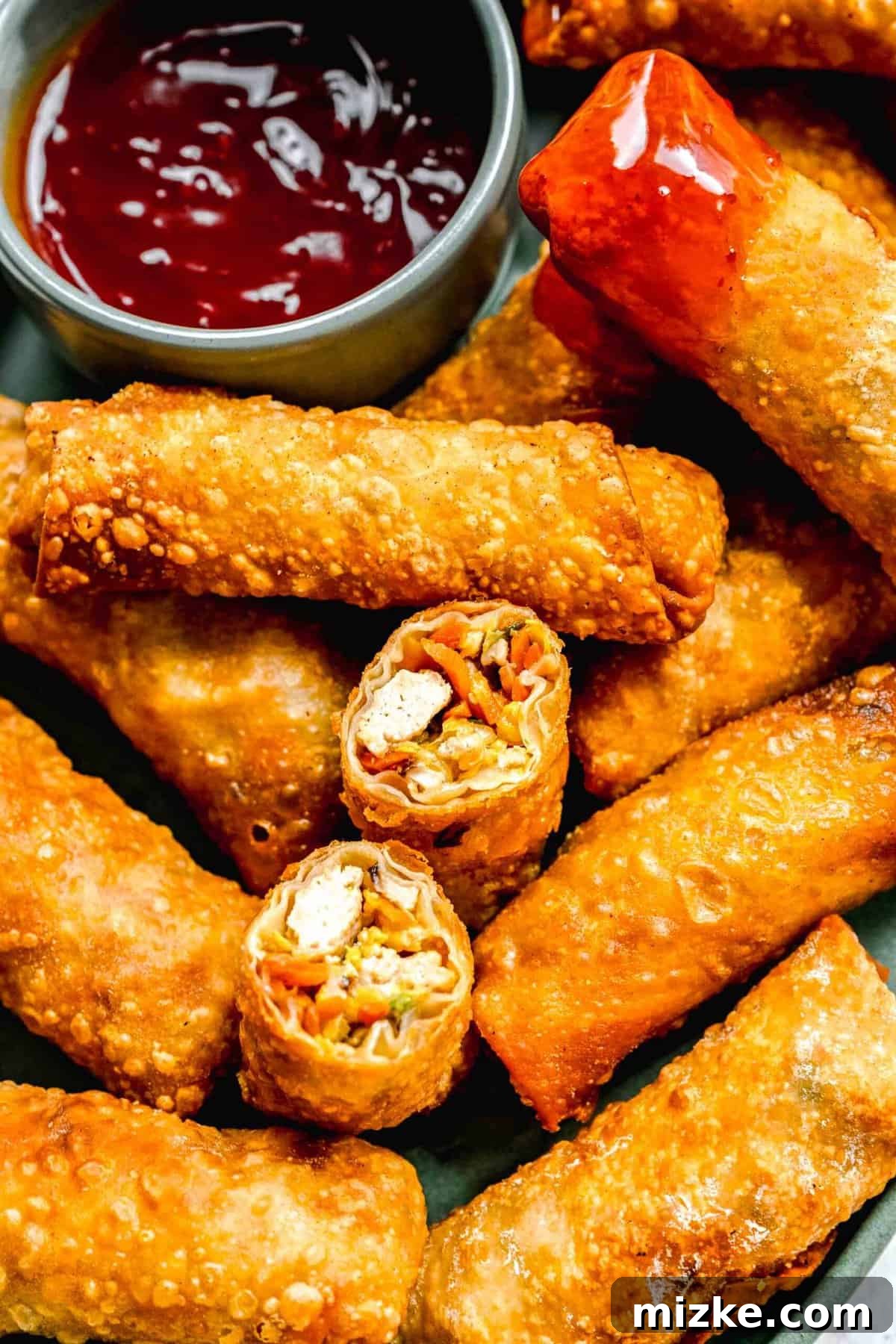 Crispy golden spring rolls on a plate with dipping sauce; one spring roll cut in half and another dipped in sauce.