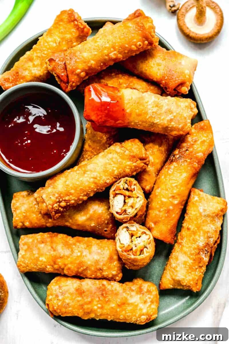 Crispy golden spring rolls on a plate with dipping sauce; one spring roll cut in half and another dipped in sauce.