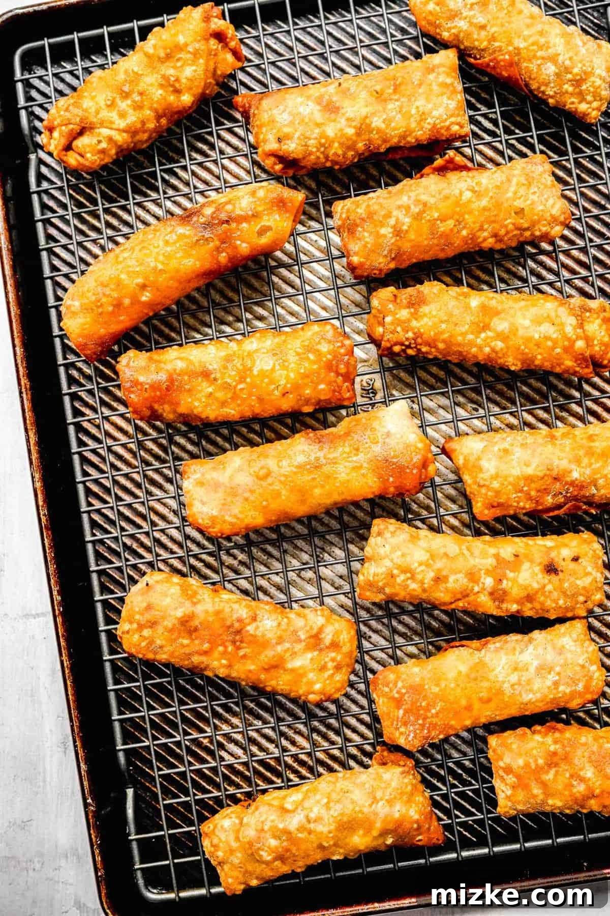 Crispy golden spring rolls arranged on a wire wrack over a baking sheet.