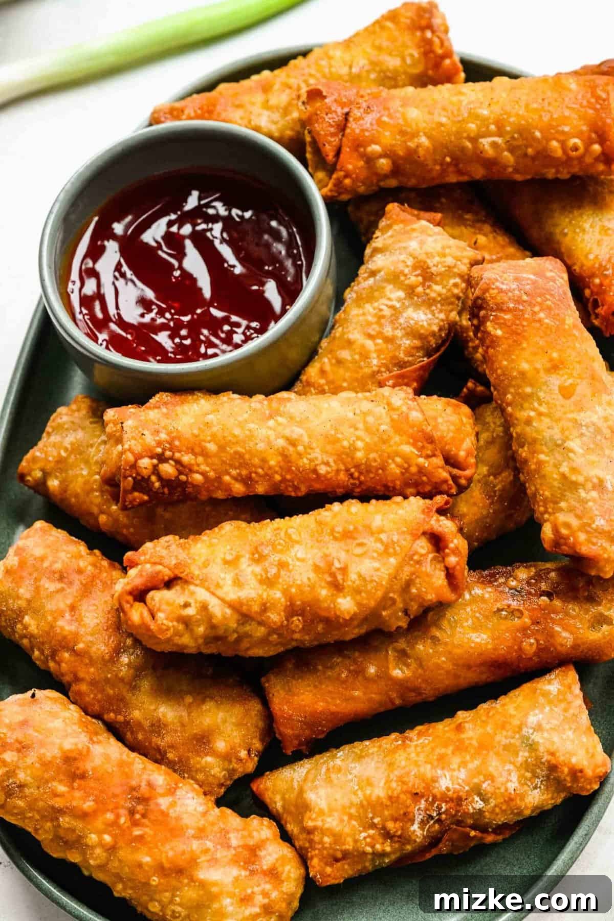 Crispy golden spring rolls on a plate with dipping sauce.