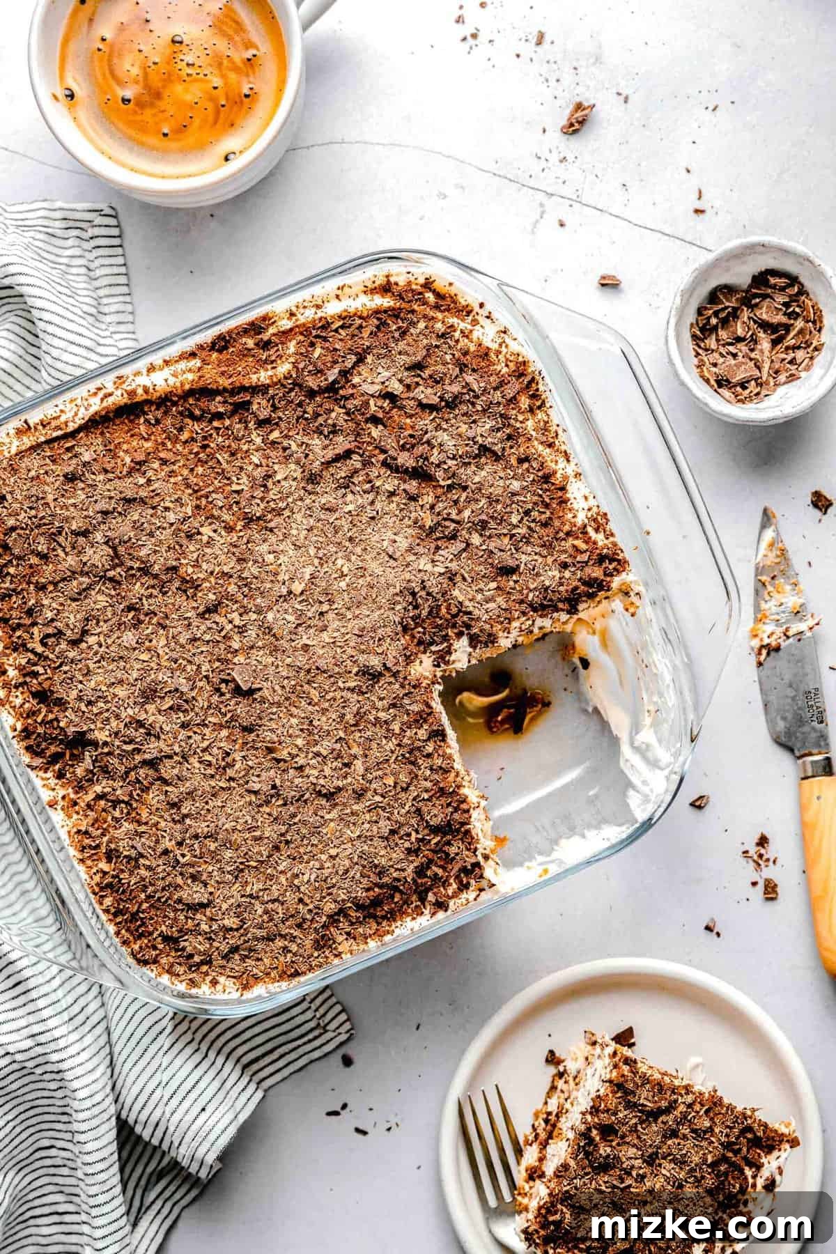 This simple tiramisu is made up of spongy, espresso-soaked ladyfingers layered with a cloudy, creamy mascarpone filling. A baking pan of tiramisu with a slice taken out of it near a cup of espresso and a bowl of chopped chocolate.
