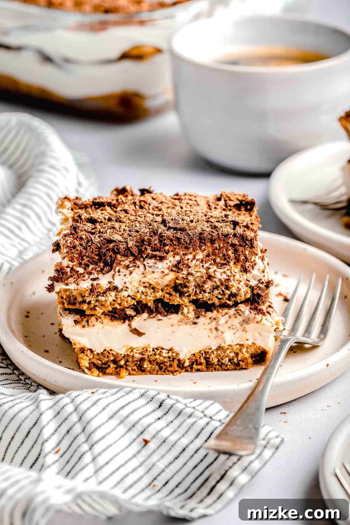 This simple tiramisu is made up of spongy, espresso-soaked ladyfingers layered with a cloudy, creamy mascarpone filling. A slice of tiramisu on a plate with a fork near a cup of espresso.