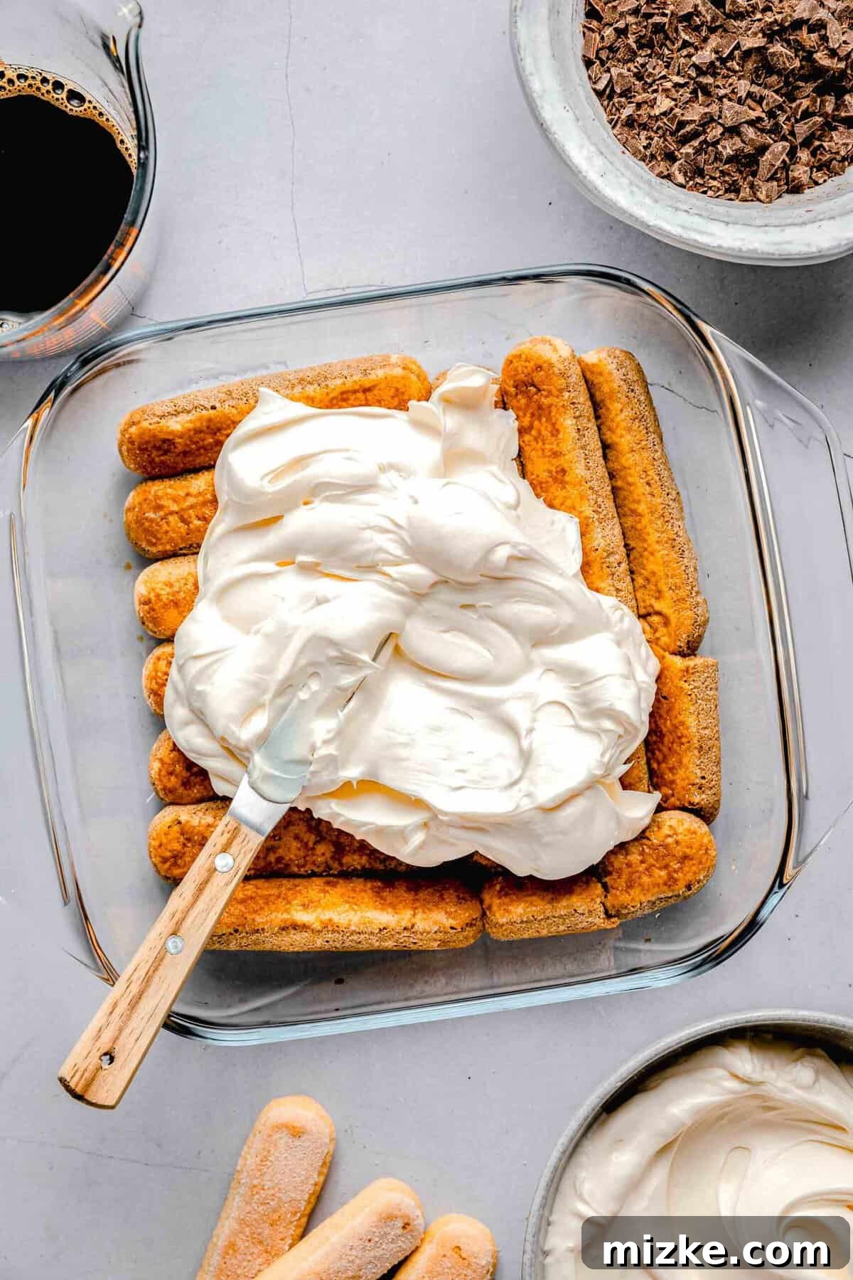 This simple tiramisu is made up of spongy, espresso-soaked ladyfingers layered with a cloudy, creamy mascarpone filling. Spreading mascarpone filling over espresso soak lady fingers in a baking pan.