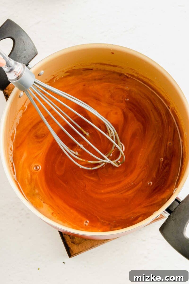 The exquisite sweet and sour sauce gently simmers, thickening to a luscious glaze that will perfectly coat every ingredient, ready to transform your dish. The homemade sweet and sour sauce being whisked to perfection in a saucepan, developing a rich, glossy, and thick texture as it simmers.