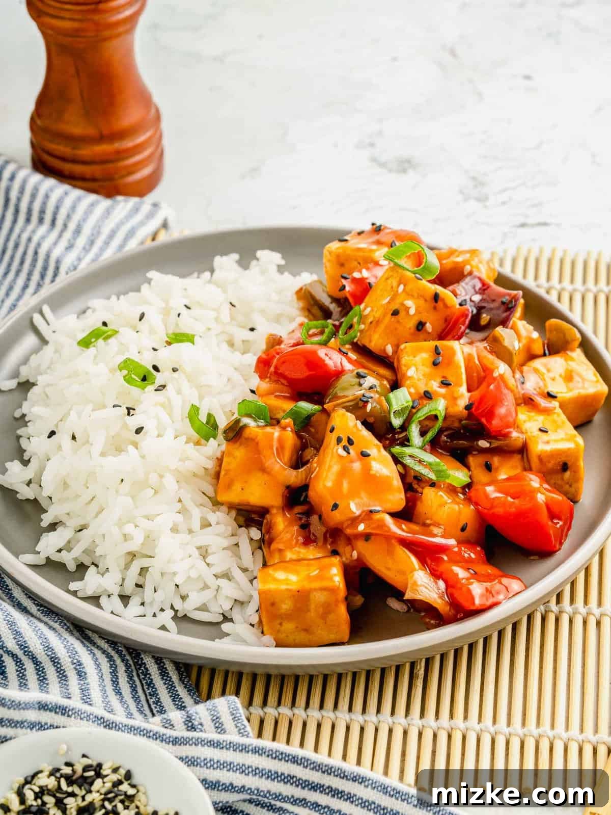 Indulge in a delicious, well-rounded meal featuring saucy sweet and sour tofu paired perfectly with a generous portion of steaming white rice. A hearty serving of sweet and sour tofu and fluffy white rice presented appealingly on a clean, round plate, ready to be enjoyed.