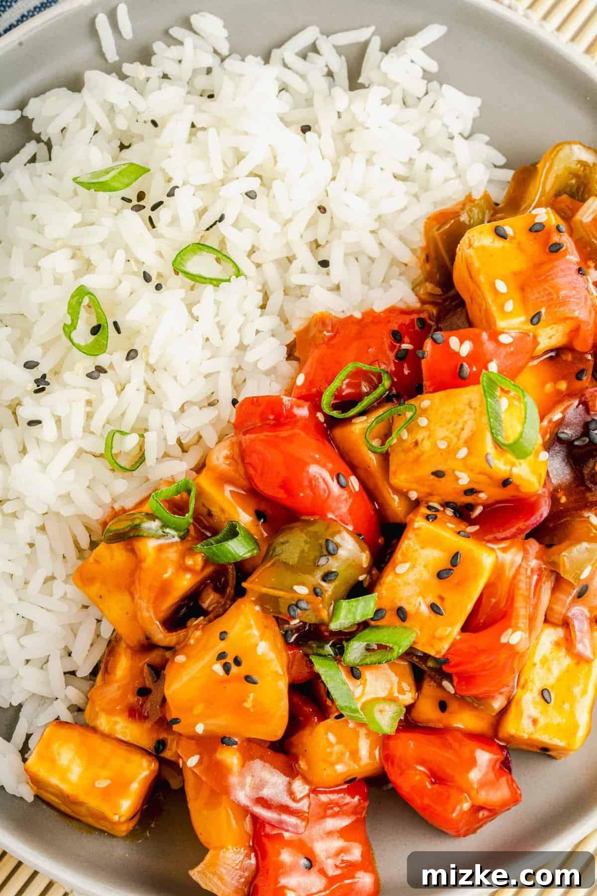 Savor a balanced and delightful meal: succulent crispy sweet and sour tofu paired elegantly with a fluffy serving of white rice. A close-up shot of crispy sweet and sour tofu generously coated in sauce, served alongside perfectly steamed white rice on a round plate, inviting to be savored.