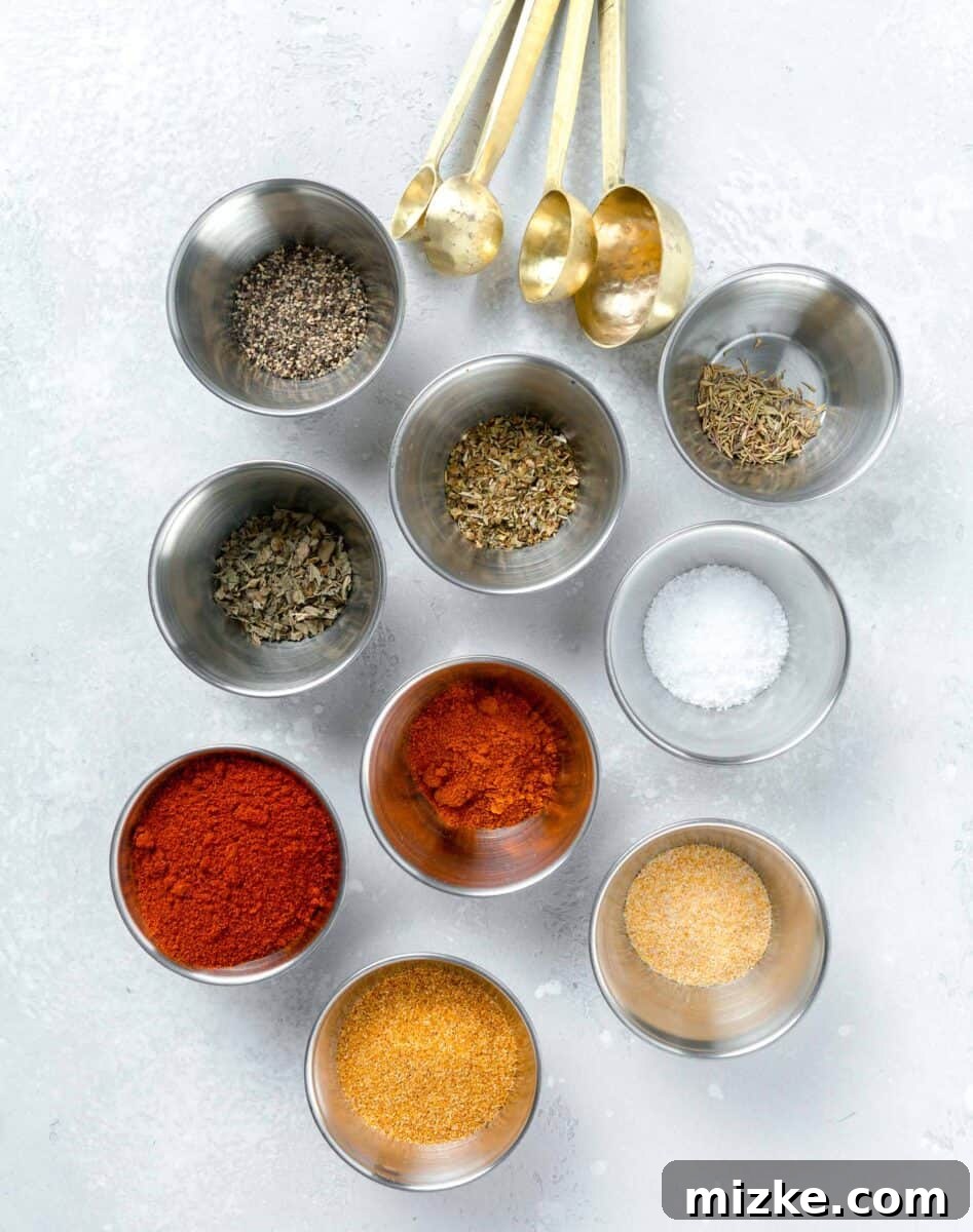 Various individual spices and dried herbs laid out on a clean white surface, showcasing the distinct colors and textures of smoked paprika, cayenne pepper, onion powder, garlic powder, black pepper, kosher salt, dried oregano, dried thyme, and dried basil – all components for blackening seasoning.