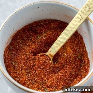 A bowl of blackening seasoning with a gold 1/4 teaspoon spoon inside next to blackening seasoning on the table