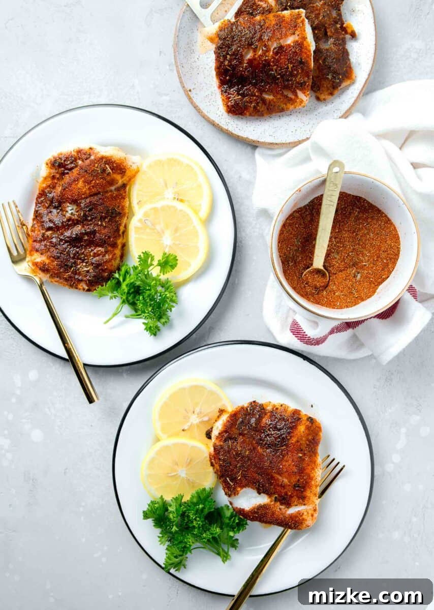 Cajun Spiced Cod Fillet 2 blackened cod on white and black rimmed plates with lemon slices and parsley next to a bowl of blackening seasoning