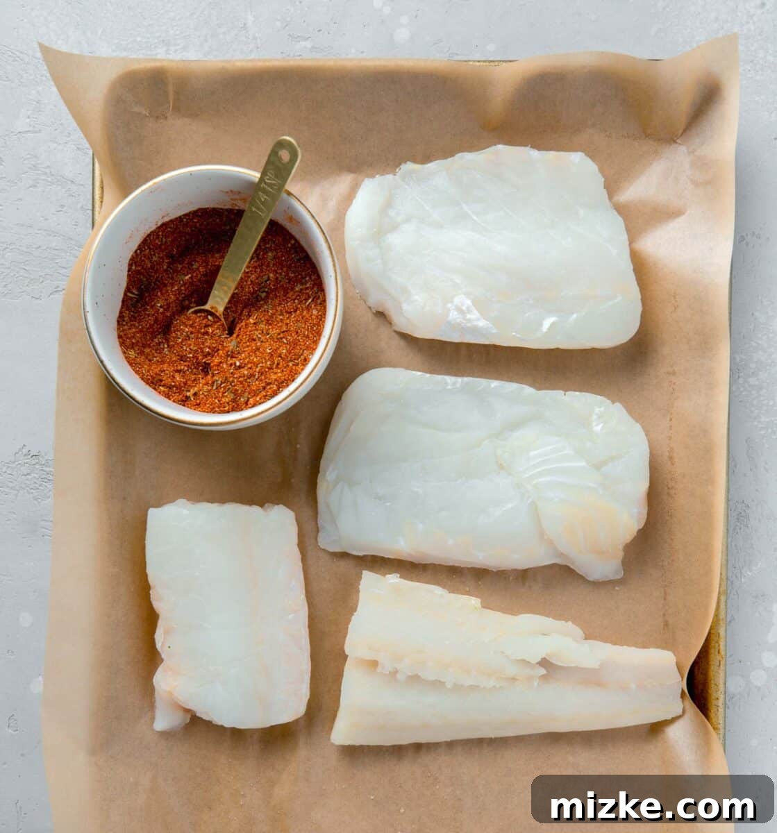 Cajun Spiced Cod Fillet 4 cod fillets next to a bowl of blackening seasoning on a parchment lined baking sheet