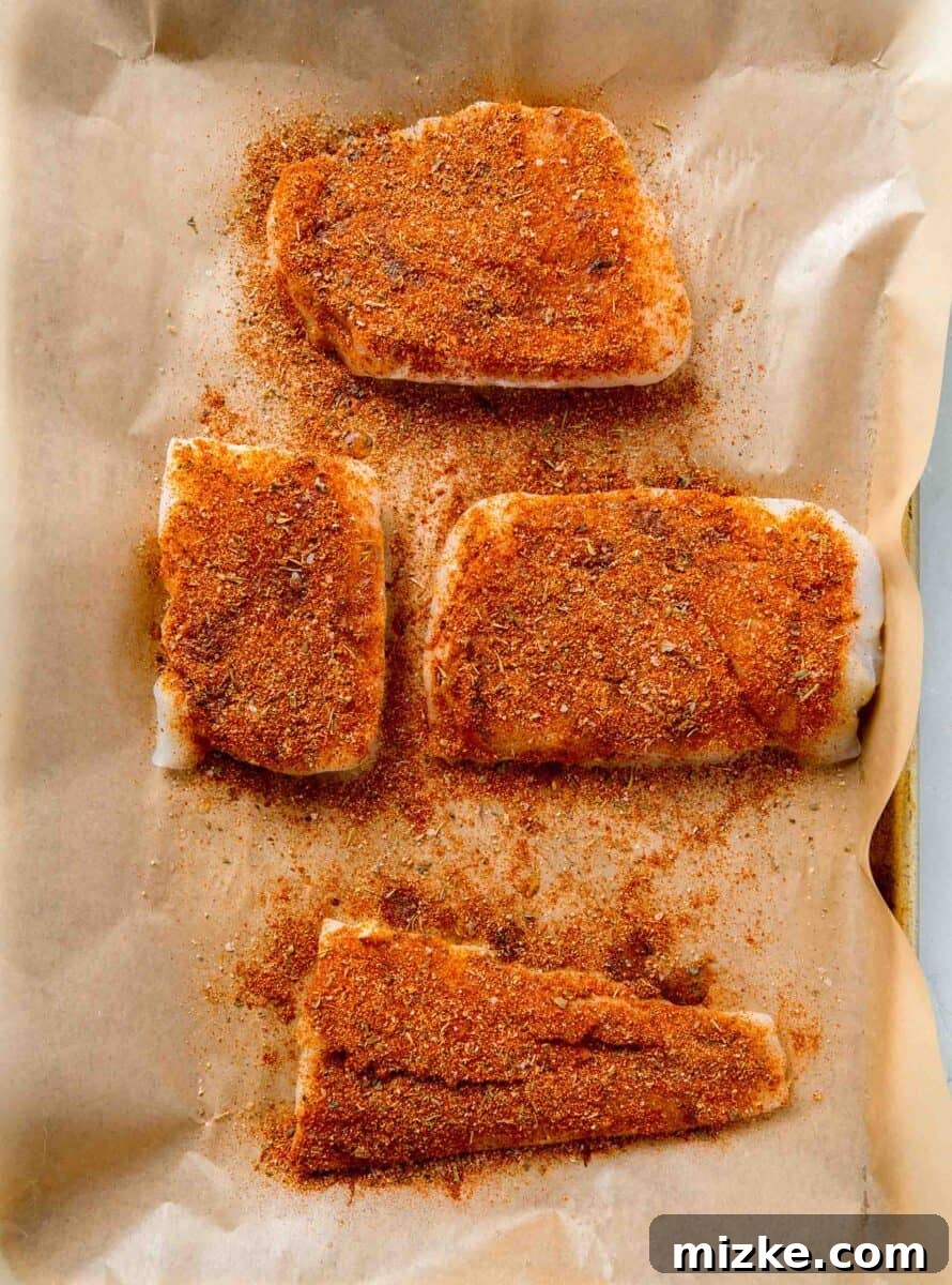 Cajun Spiced Cod Fillet 5 cod fillets coated with blackening seasoning on a parchment lined baking sheet