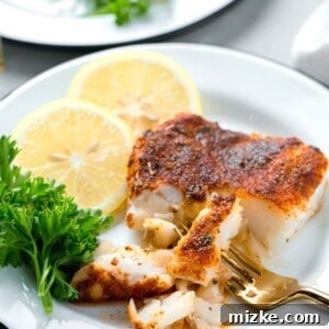 a gold fork breaking apart the tender blackened cod filet on a plate