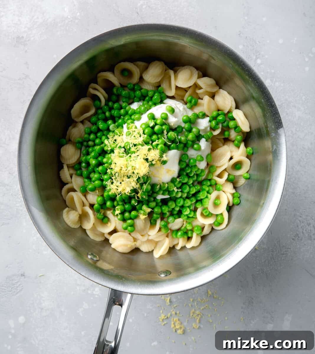Creamy Lemon Ricotta One-Pot Pasta 5 Green peas and fresh lemon zest sprinkled over ricotta cheese and cooked pasta in a stainless steel pot, ready to be mixed.