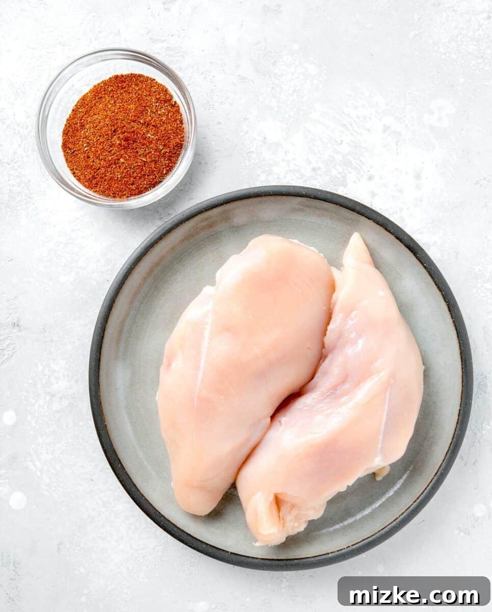 Ultimate Air Fryer Blackened Chicken 3 A selection of ingredients for air fryer blackened chicken, including raw boneless, skinless chicken breasts and a bowl of rich blackening seasoning.