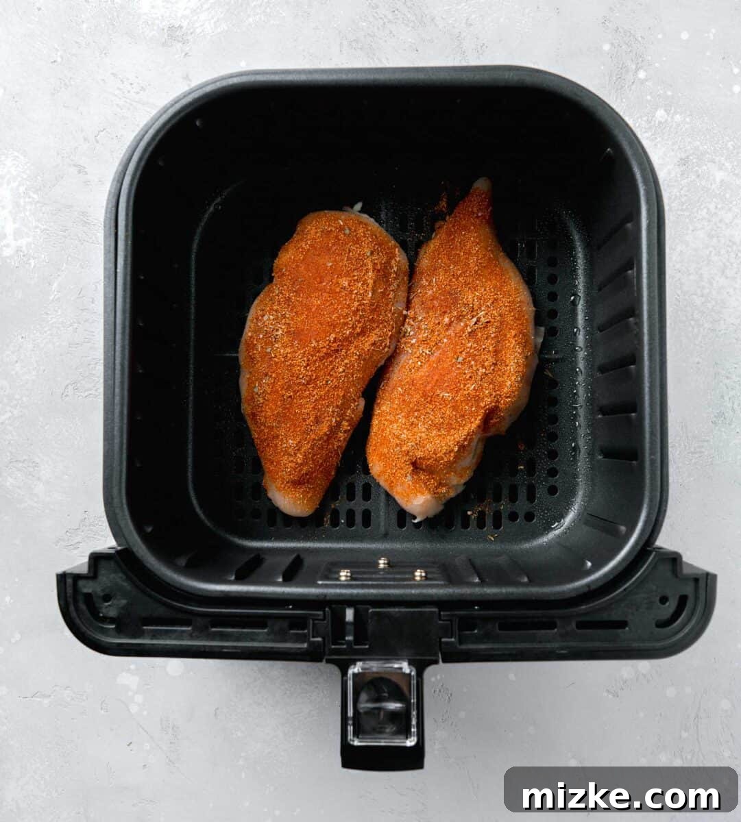 Ultimate Air Fryer Blackened Chicken 4 Raw chicken breasts generously coated in blackening seasoning, placed in the basket of an air fryer, ready for cooking.