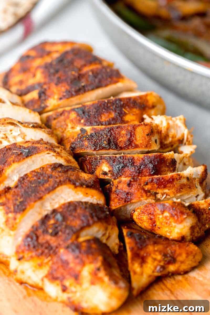 Ultimate Air Fryer Blackened Chicken 6 A close-up view of air fryer blackened chicken on a wooden cutting board, highlighting the rich, dark blackening seasoning and the textured surface.