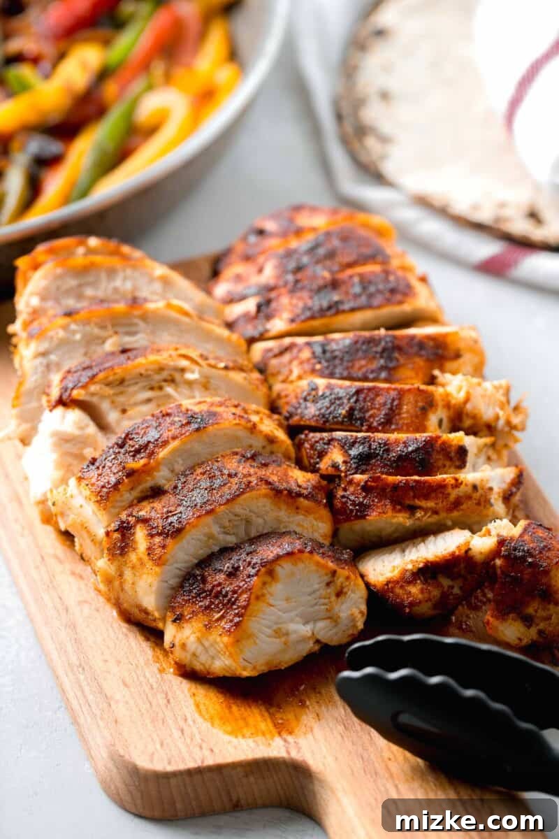 Ultimate Air Fryer Blackened Chicken 7 Perfectly sliced air fryer blackened chicken pieces arranged on a wooden cutting board, ready to be served or added to other dishes. Black tongs are nearby.