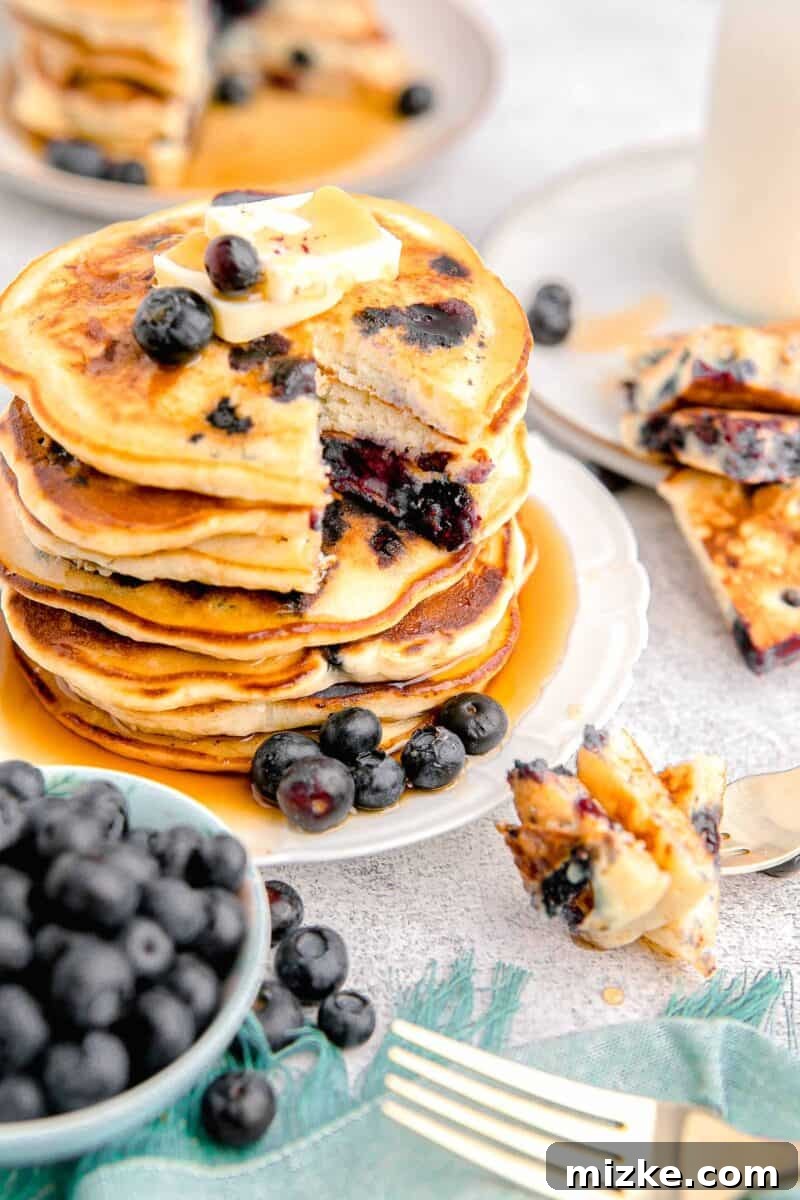 Sweet Blueberry Stacks 12 A stunning stack of golden-brown blueberry pancakes, beautifully presented with a dollop of butter, a sprinkle of fresh blueberries, and a generous pour of golden maple syrup.
