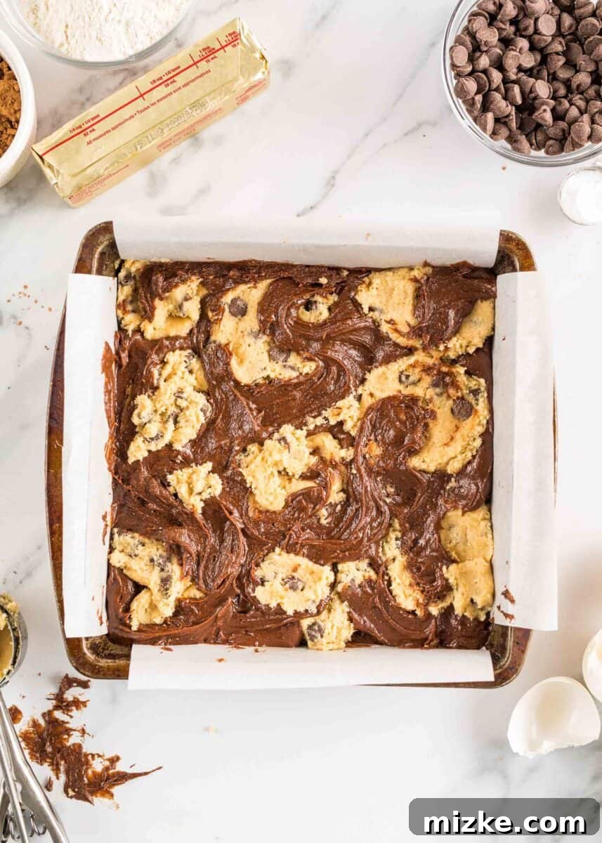 Brownie Cookie Fusion 8 Unbaked brookies, with brownie batter as the base and dollops of cookie dough swirled on top, are carefully arranged in a square baking dish, ready for the oven.