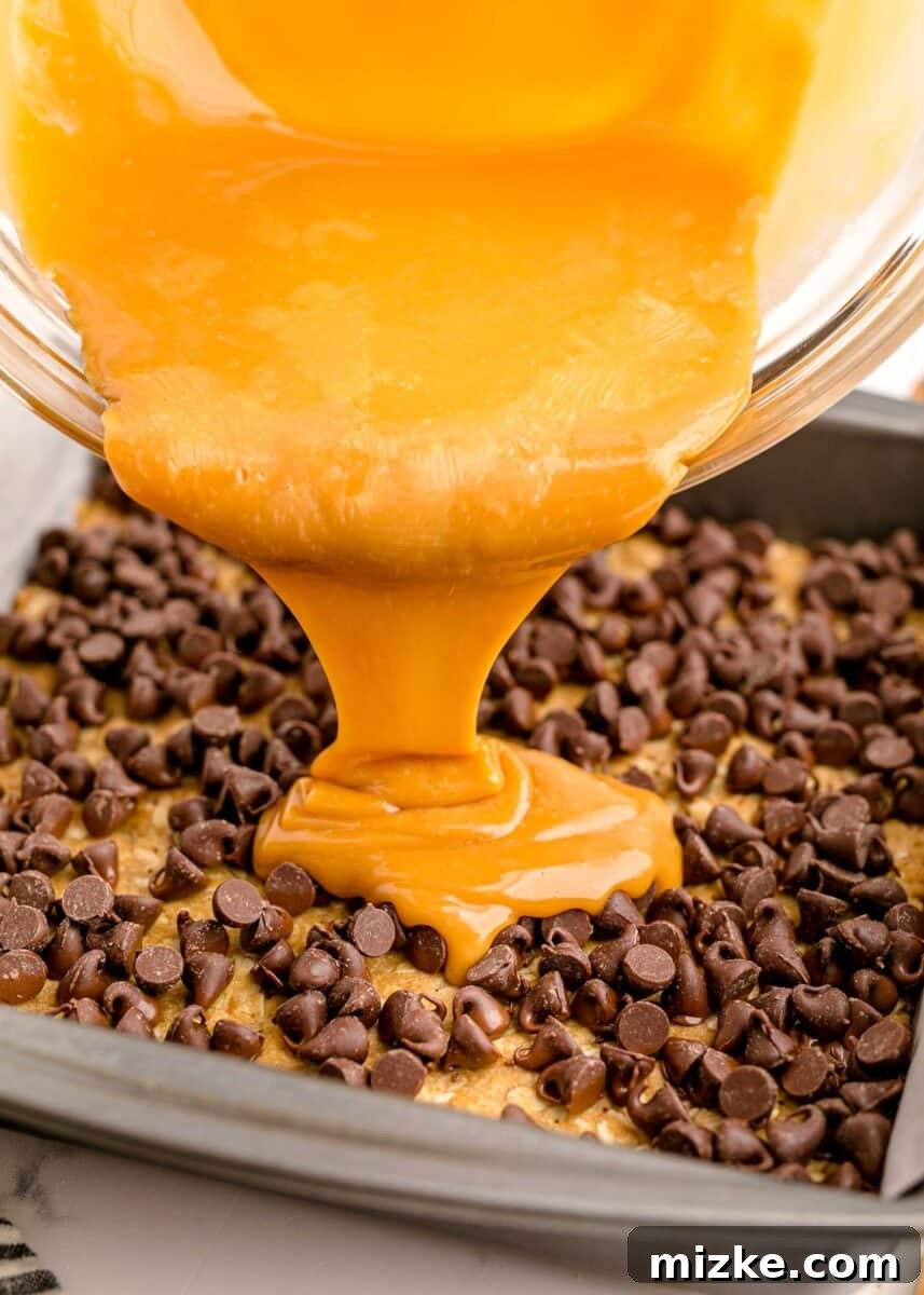 The Carmelitas Legacy 8 Warm caramel sauce is being generously poured over a layer of semi-sweet chocolate chips on the baked oat crust.