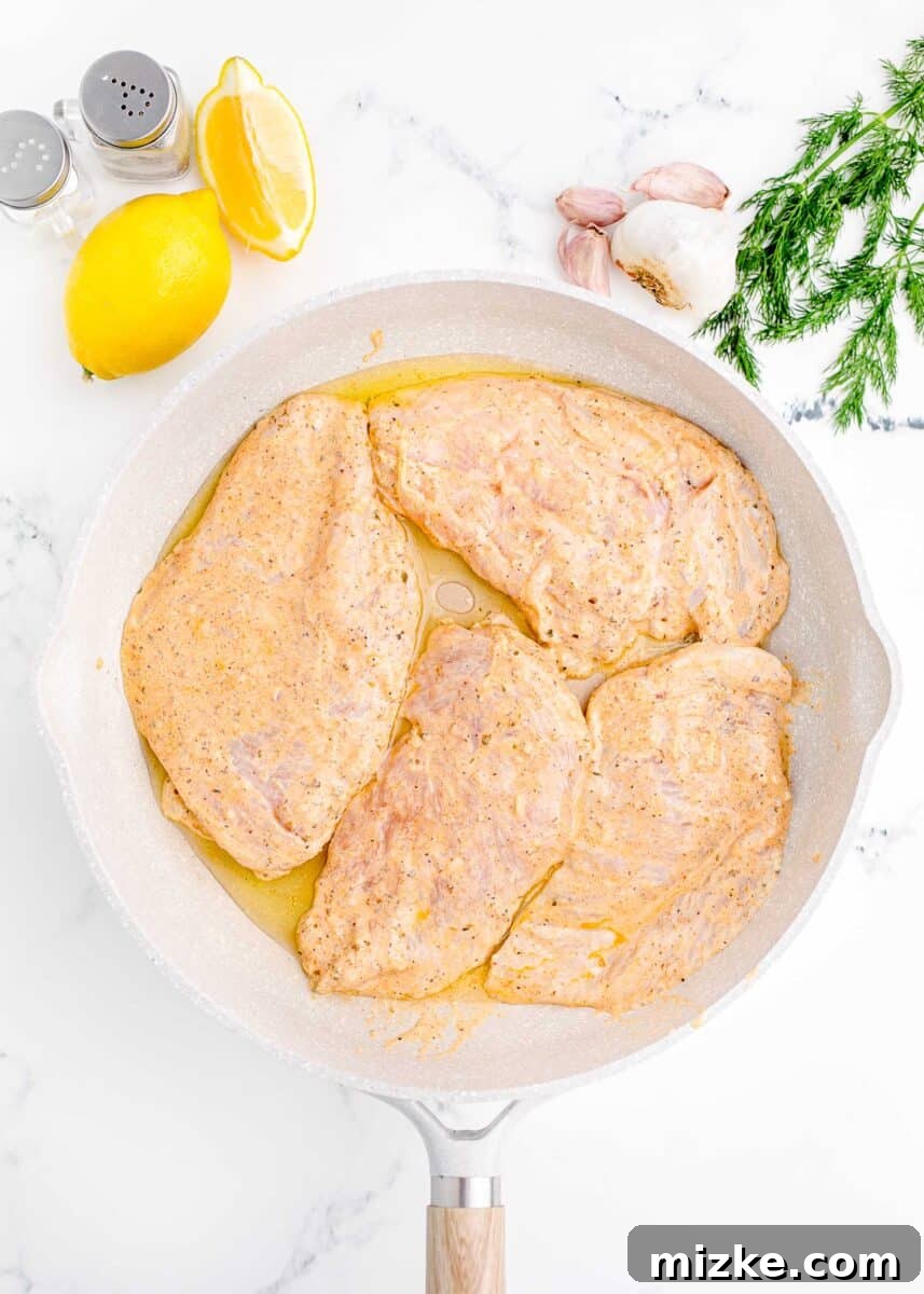 Mediterranean Chicken Wraps 6 uncooked chicken breasts are placed in a white skillet.