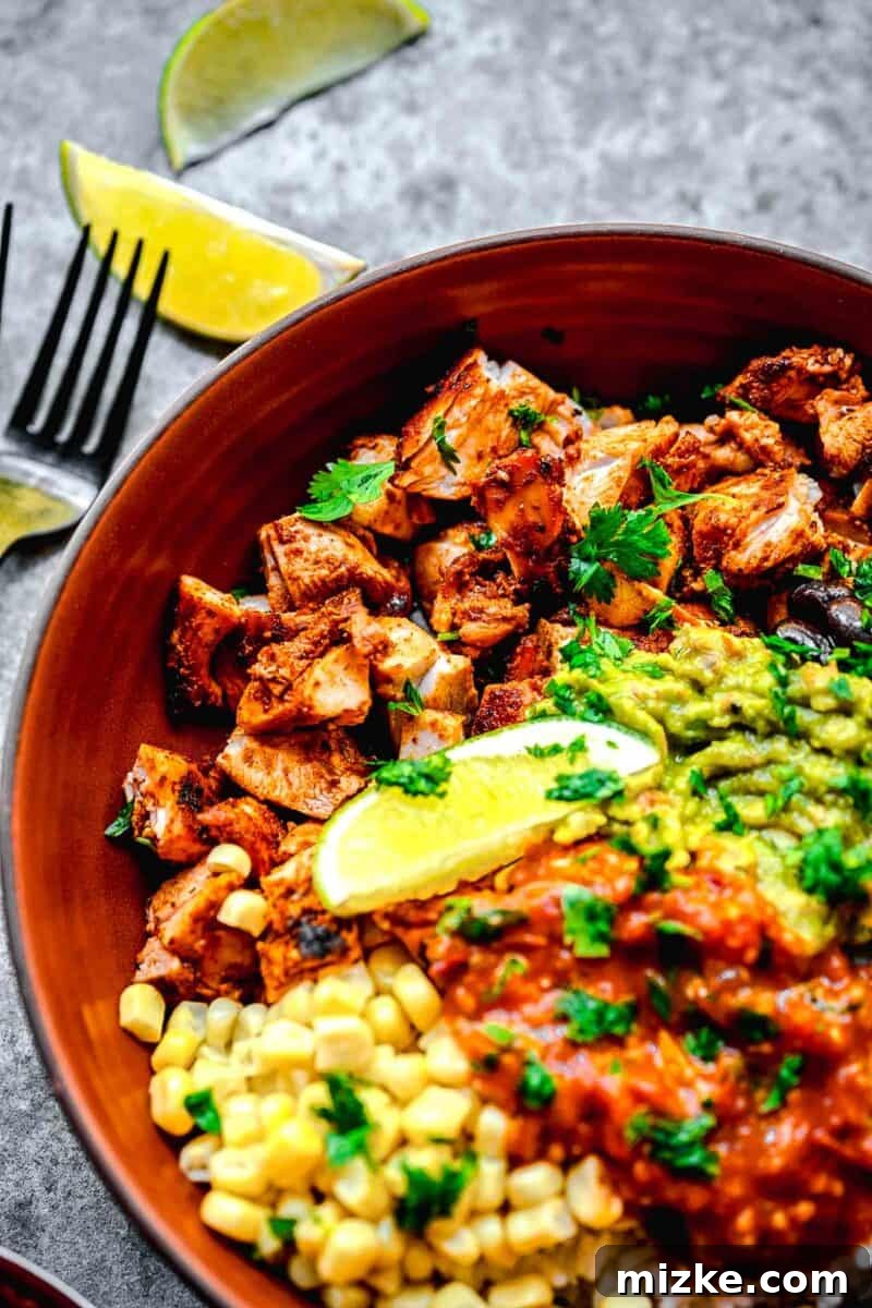 Smoky Chipotle Grilled Chicken 3 A full, vibrant Chipotle Chicken burrito bowl is meticulously arranged next to a fresh lime wedge and a fork, ready to be enjoyed.