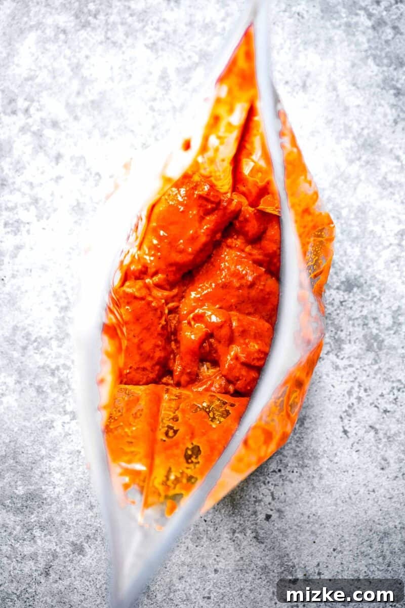 Smoky Chipotle Grilled Chicken 5 A sealed plastic bag is filled with boneless, skinless chicken, thoroughly coated in a rich, red-orange marinade, ready for refrigeration.