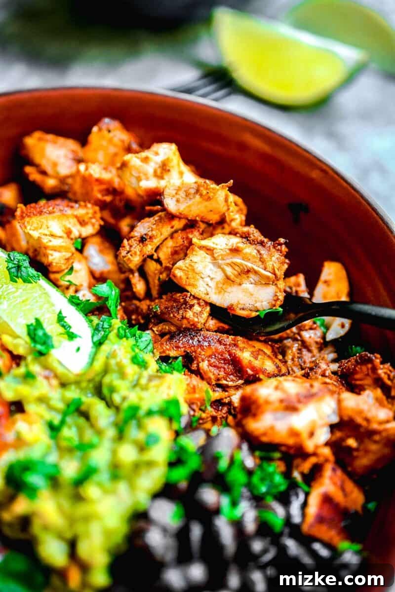 Smoky Chipotle Grilled Chicken 8 Succulent chicken, hearty beans, and creamy guacamole are beautifully arranged on a bed of fluffy white rice in a rustic brown bowl.